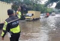 tampak polisi di lokasi banjir mengatur lalulintas agar kendaraan tidak mogok dan lalulintas kembali lancar.